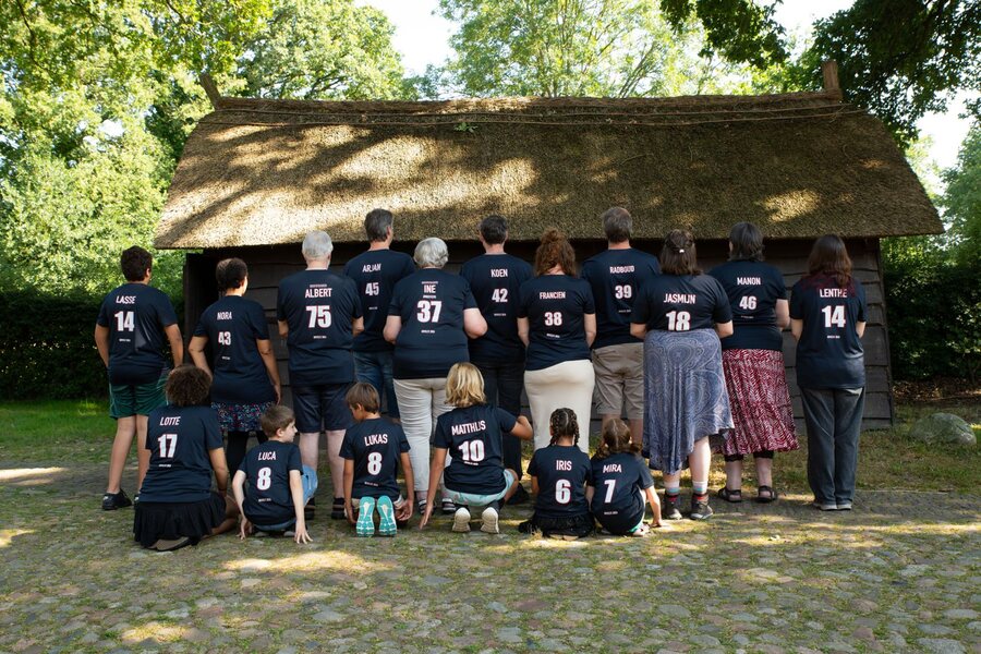 Alle zeventien familieleden van achteren voor de rieten schuur, met ieders naam en leeftijd gedrukt op de rug van hun donkerblauwe Team Geven-shirt