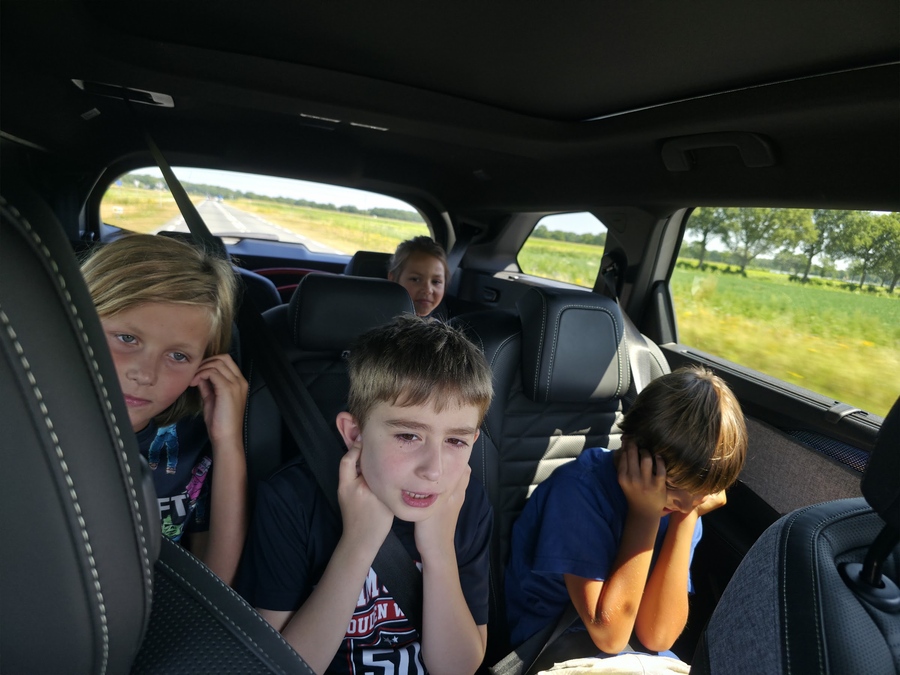 Vier kinderen op de achterbank van de auto met het hoofd in hun handen, op weg naar de volgende stop