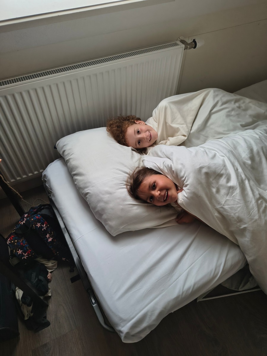 Twee kinderen liggen giechelend naast elkaar onder de dekens in bed
