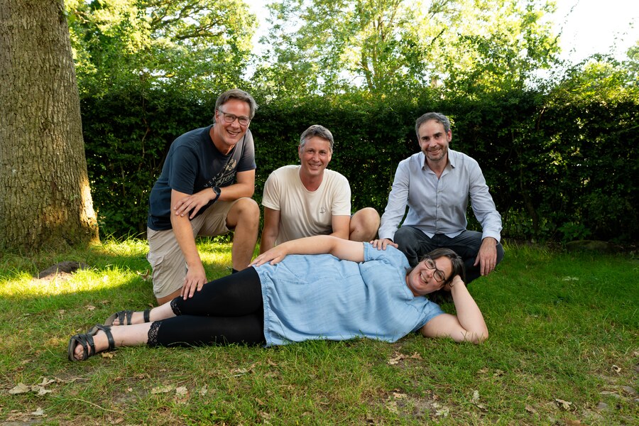Manon ligt lachend in het gras, Arjan, Koen en Radboud hurken lachend naast haar