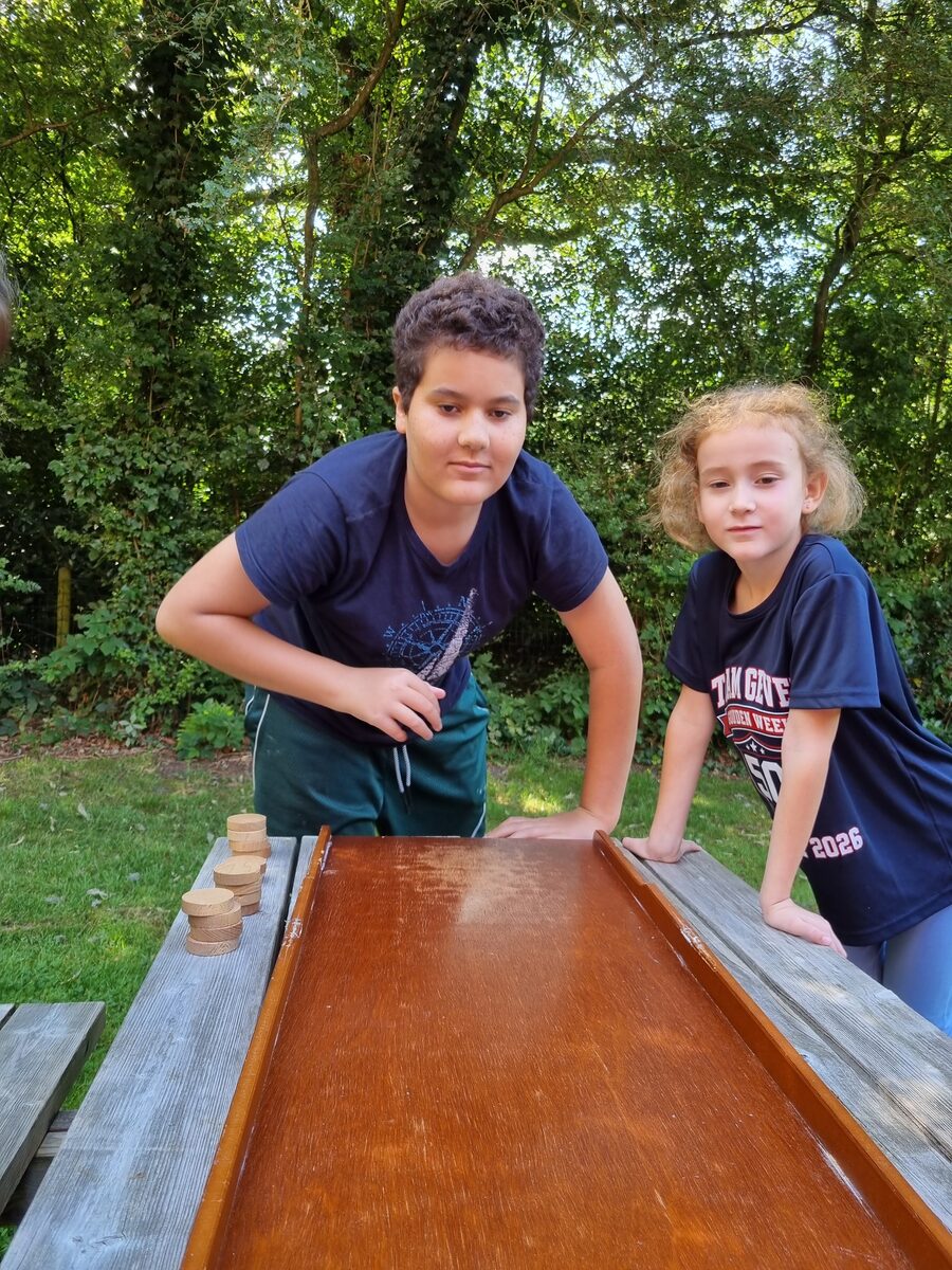 Twee kinderen gebogen over een sjoelbak op de picknicktafel in de tuin