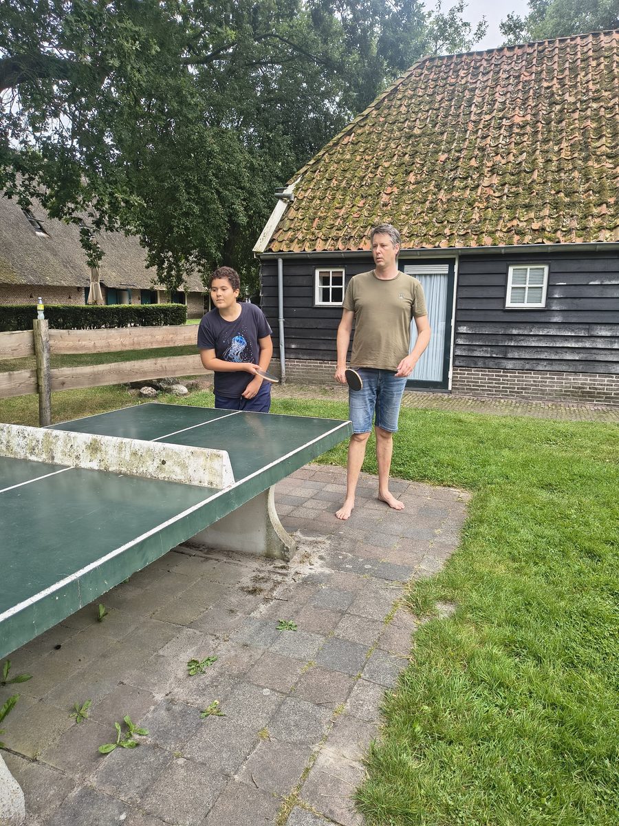 Een tienerjongen en een oudere man spelen tafeltennis aan de betonnen tafel buiten