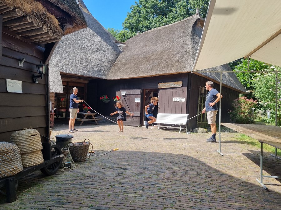 Twee volwassenen draaien een lang springtouw, twee kinderen springen ertussen