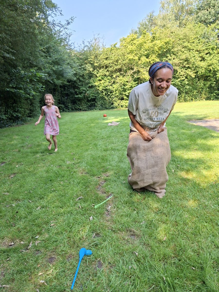 Nora springt lachend in een jute zak over het gras, een klein meisje rent achter haar aan