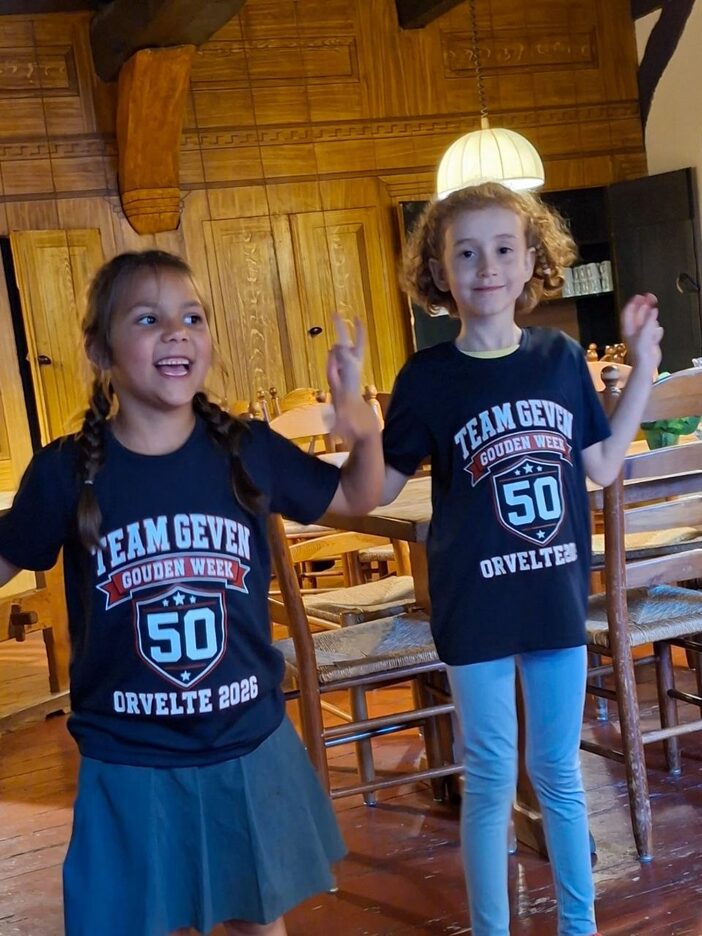 Iris en Mira in hun donkerblauwe shirt met op de borst TEAM GEVEN, een rode banier met GOUDEN WEEK, een wapenschild met een grote 50, en daaronder ORVELTE 2026
